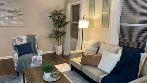 A living room with a sofa, armchair, coffee table, and a potted plant.