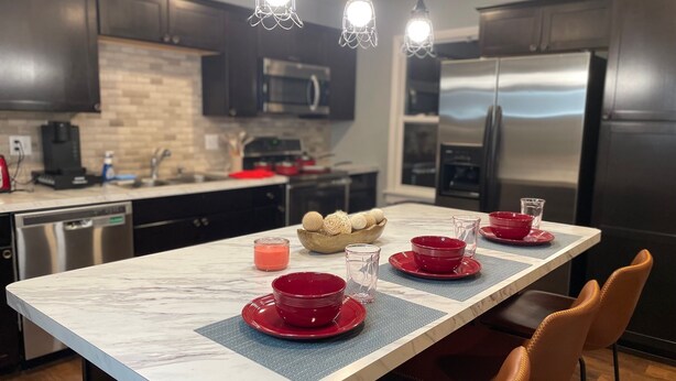 A modern kitchen with dark cabinets, a marble countertop, and a central island with red bowls and glasses.