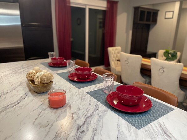 Una mesa de comedor puesta con platos, tazones y una vela rojos.