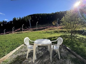 A table with two chairs in a grassy area with a forested hill in the background.