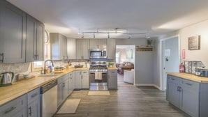 Una cocina moderna con gabinetes grises, electrodomésticos de acero inoxidable y encimera de madera.
