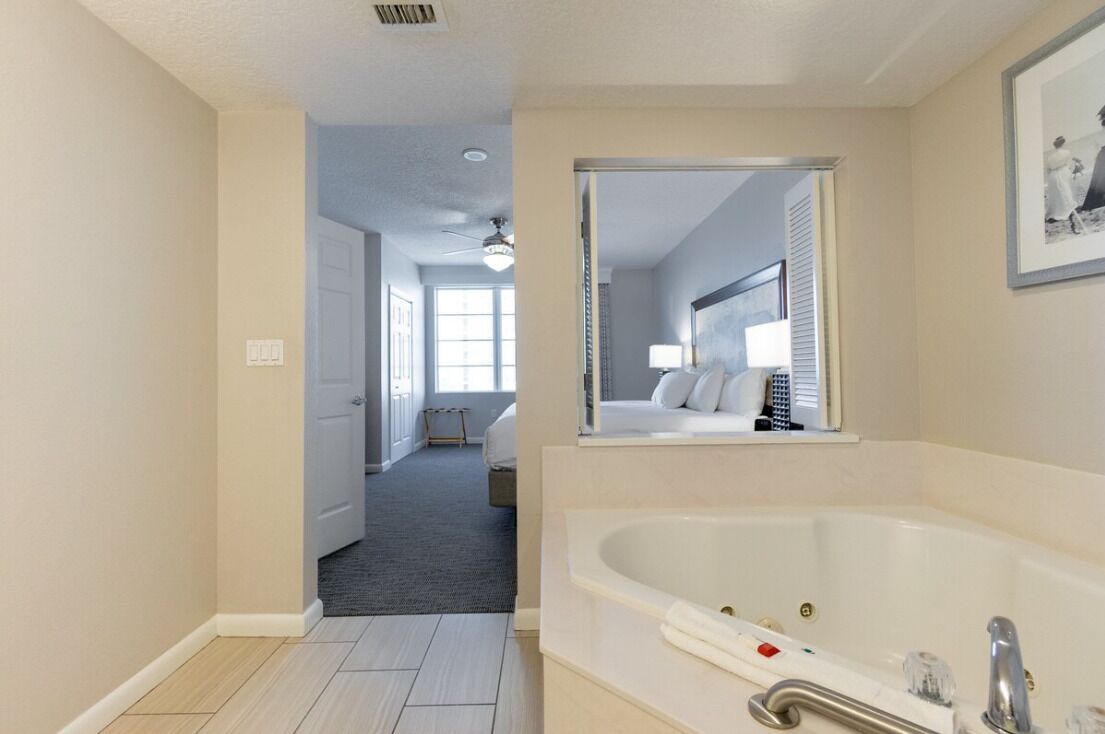 A modern bathroom with a large bathtub, a mirror, and a door leading to a bedroom.