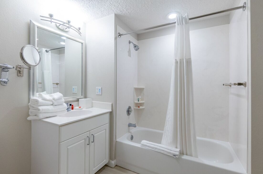 Un baño con tocador blanco, un espejo, una bañera y una cortina de ducha.