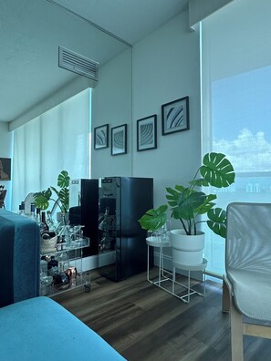 A modern living room with a large window, a black refrigerator, a blue sofa, and a potted monstera plant.