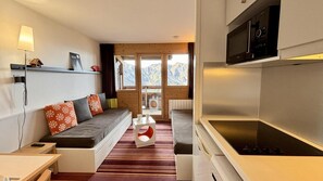 Sala de estar moderna com sofá, uma mesinha, área de cozinha com micro-ondas e vista para as montanhas pela janela.