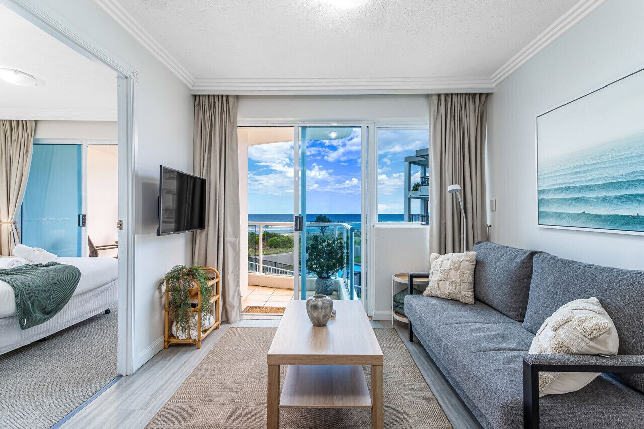 A modern hotel room with a balcony, a sofa, a TV, and a view of the ocean.