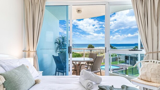 A hotel room with a bed, a view of the ocean, a balcony with a table and chairs, and a pool. - Surf Watch Palm Beach (Palm Beach)