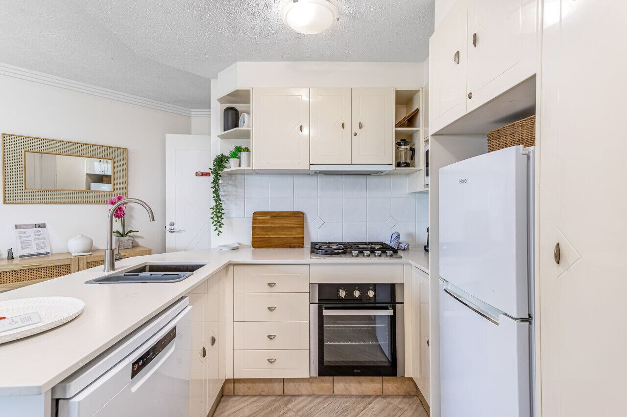 A modern kitchen with white cabinetry, a built-in oven, a sink, and a refrigerator.