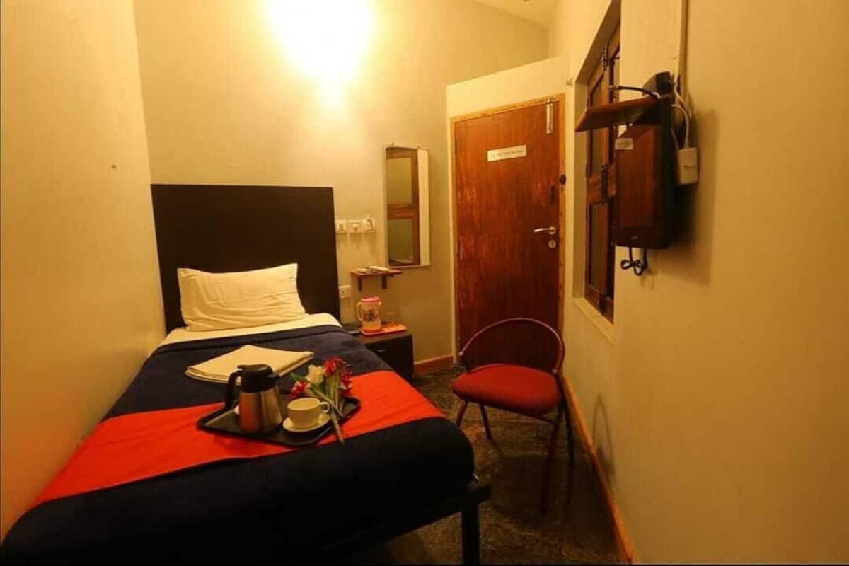 Une chambre d’hôtel avec un lit, une chaise, une table de chevet avec une lampe et une porte.