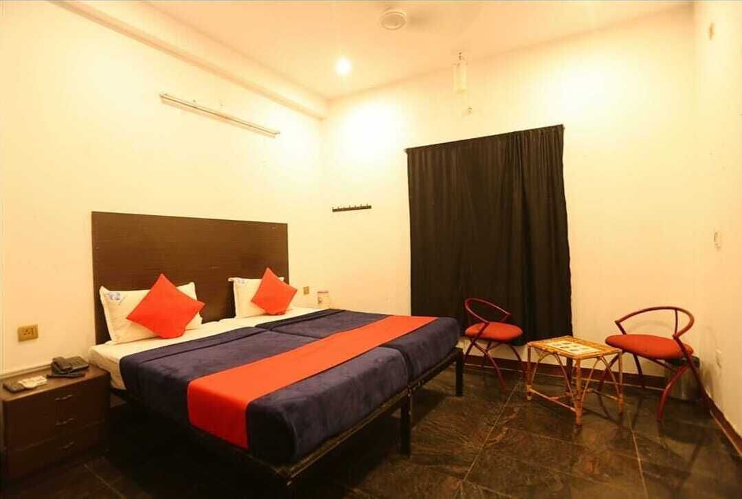 A hotel room with a bed, two chairs, a small table, and a nightstand.