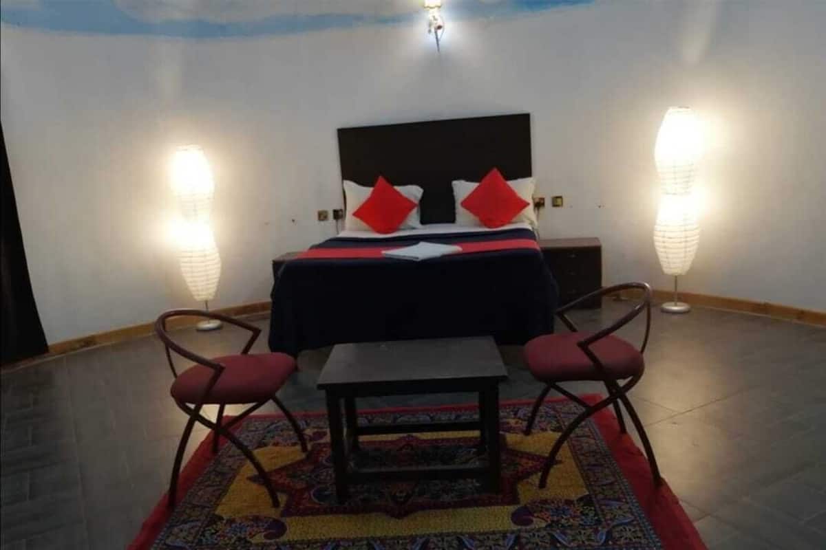 Une chambre d’hôtel comprenant un lit, deux chaises, une petite table et deux lampes fixées au mur.