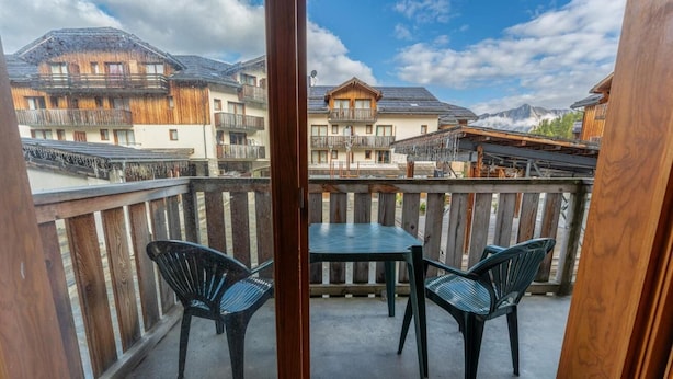 A balcony with a table and two chairs, overlooking a mountainous landscape with wooden buildings.