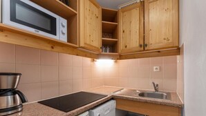A compact kitchen with wooden cabinets, a microwave, a coffee maker, a dishwasher, and a sink.