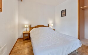 A bedroom with a wooden bed, two bedside tables with lamps, and a wooden wardrobe. - 40m from ski slopes, 1st floor, fitness, swimming pool, sauna, balcony, tv, ski locker, 37m² (Les Orres)