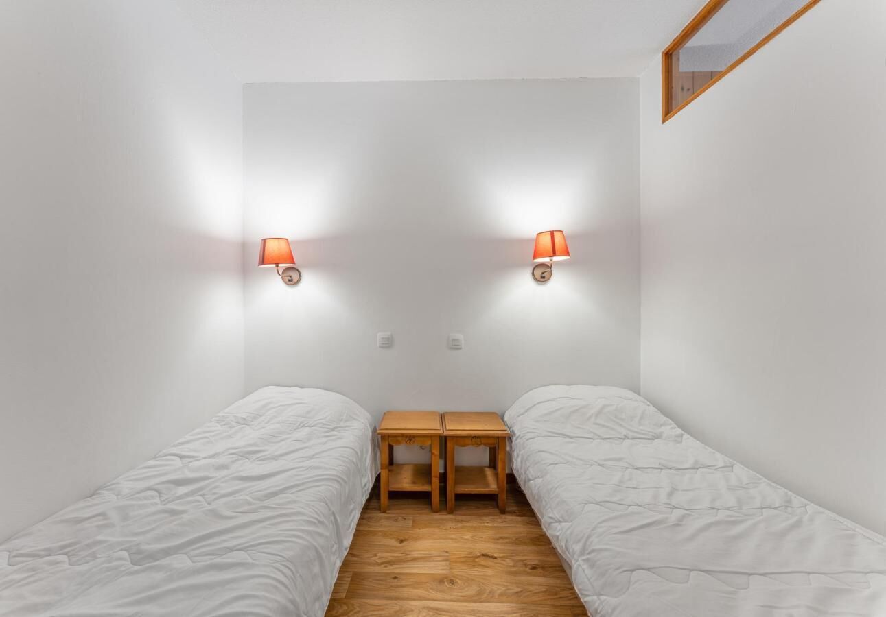 Un alojamiento pequeño con una sola habitación, dos camas individuales, una mesita de noche de madera y dos lámparas fijadas a la pared.