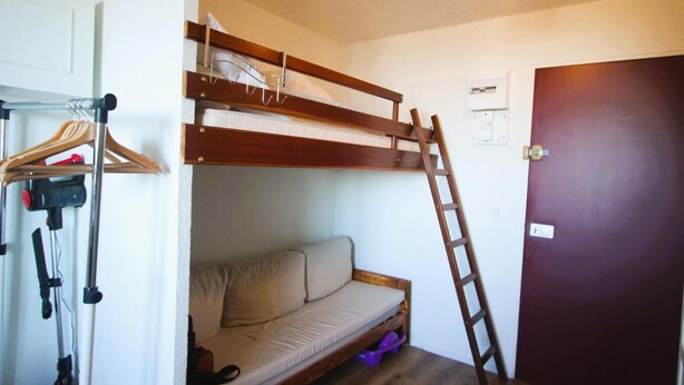 Una litera con escalera, un sofá, un perchero y una puerta.