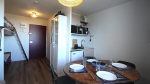 Una cocina compacta con refrigerador, microondas y un lavamanos pequeño. Hay una mesa de comedor con sillas y una araña colgante.