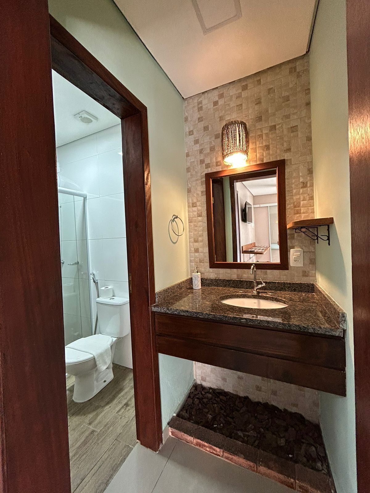 Un baño con lavamanos de encimera de granito, un espejo y una ducha visible al fondo.