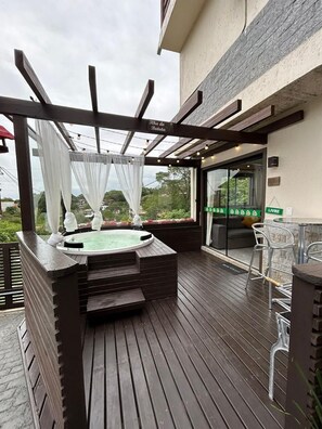 A hot tub with a pergola and white curtains, a bar area with chairs, and a view of greenery. - Pousada Morada Porto Verde (Imbituba)