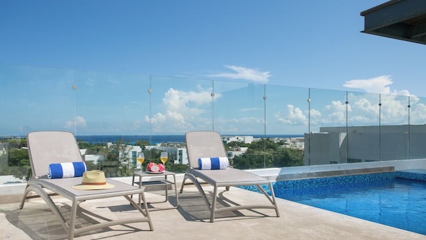 A rooftop pool area with two lounge chairs, a small table, and a clear view of the ocean and cityscape.