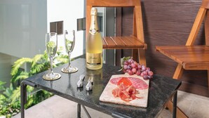 A table with a bottle of champagne, two glasses, a knife, a cutting board with sliced meats, and a bunch of grapes.