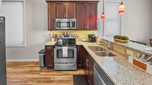 Une cuisine moderne avec des meubles en bois foncé, des appareils électroménagers en acier inoxydable, des plans de travail en granit et un lave-vaisselle intégré.