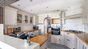 A modern kitchen with white cabinets, a wooden countertop, a built-in oven, and a stainless steel sink. - Seafront Retreat: Opulent 4BR Haven for Big Groups (Birchington-on-Sea)