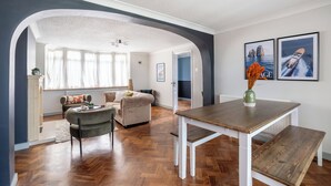 A spacious living area with a wooden herringbone floor, a dining table with benches, and a cozy seating area with a sofa and armchairs. - Seafront Retreat: Opulent 4BR Haven for Big Groups (Birchington-on-Sea)