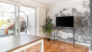 A room with a wooden floor, a large window, a black TV on a stand, and a wall with a nature-themed mural. - Seafront Retreat: Opulent 4BR Haven for Big Groups (Birchington-on-Sea)