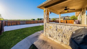 A patio area with a stone wall, a ceiling fan, and a wooden fence.