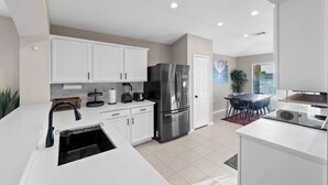 A modern kitchen with white cabinets, a stainless steel refrigerator, and a dining area with a table and chairs.