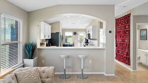 A modern kitchen with a central island, bar stools, and a red patterned wall.