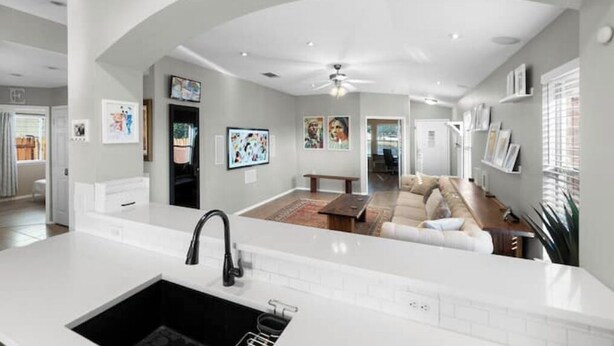 A modern kitchen with a white countertop and black sink, leading to a living area with a sofa and coffee table.
