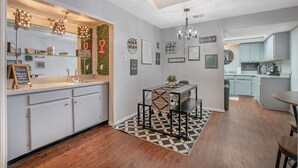 Een moderne keuken met witte kasten, een zwart-wit kleed en een eethoek met een metalen tafel en bank.