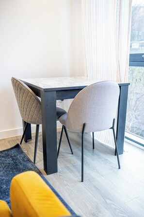 Een moderne eetruimte met een donker houten tafel en twee stoelen, waarvan één met een gewatteerd rugleuning en de ander met een gladde rugleuning.