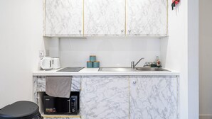 A compact kitchen with marble cabinets, a coffee maker, a microwave, and a sink.