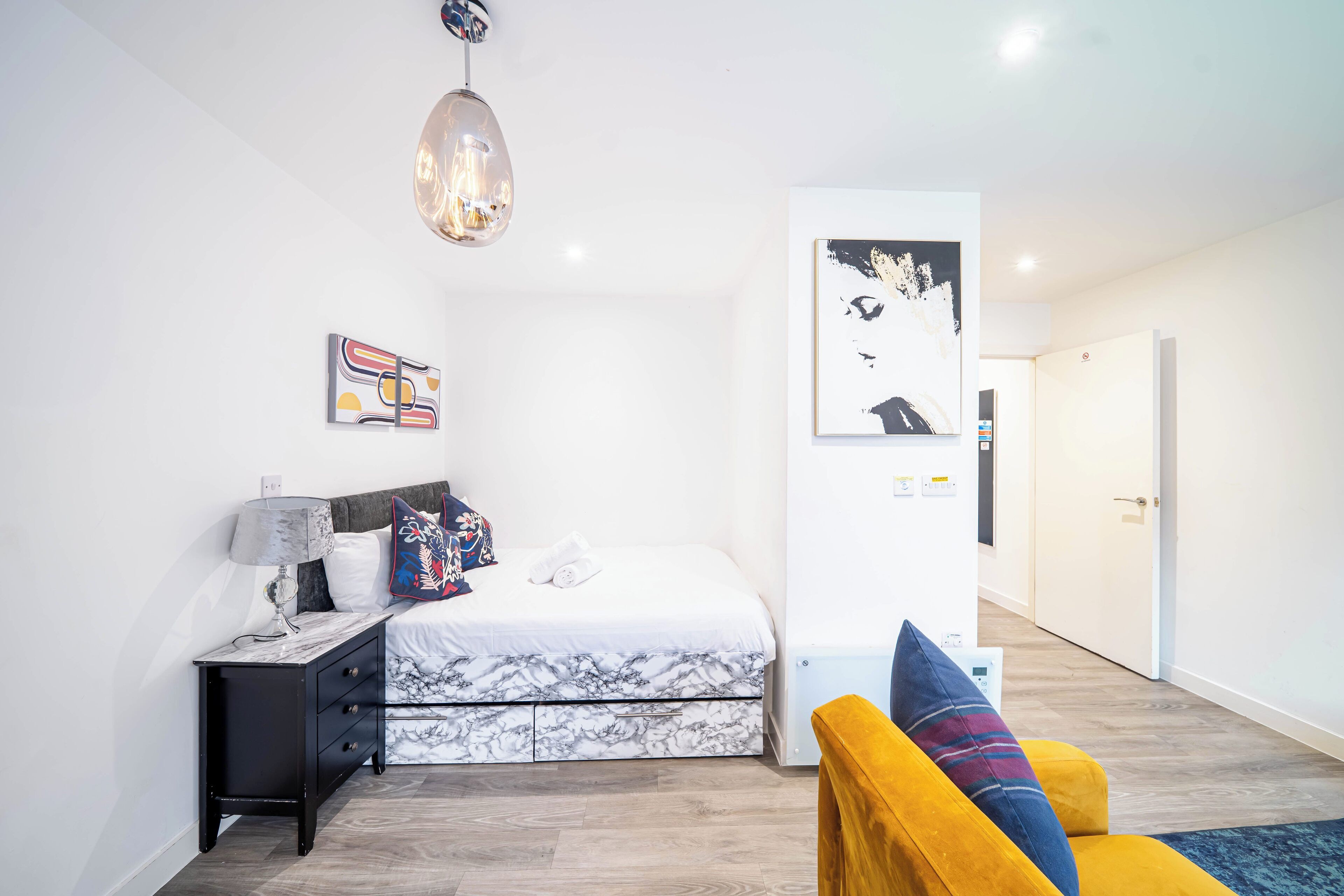 A modern bedroom with a bed, a nightstand, a lamp, a wall art piece, and a door leading to another room.