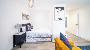 A modern bedroom with a bed, a nightstand, a lamp, a wall art piece, and a door leading to another room.