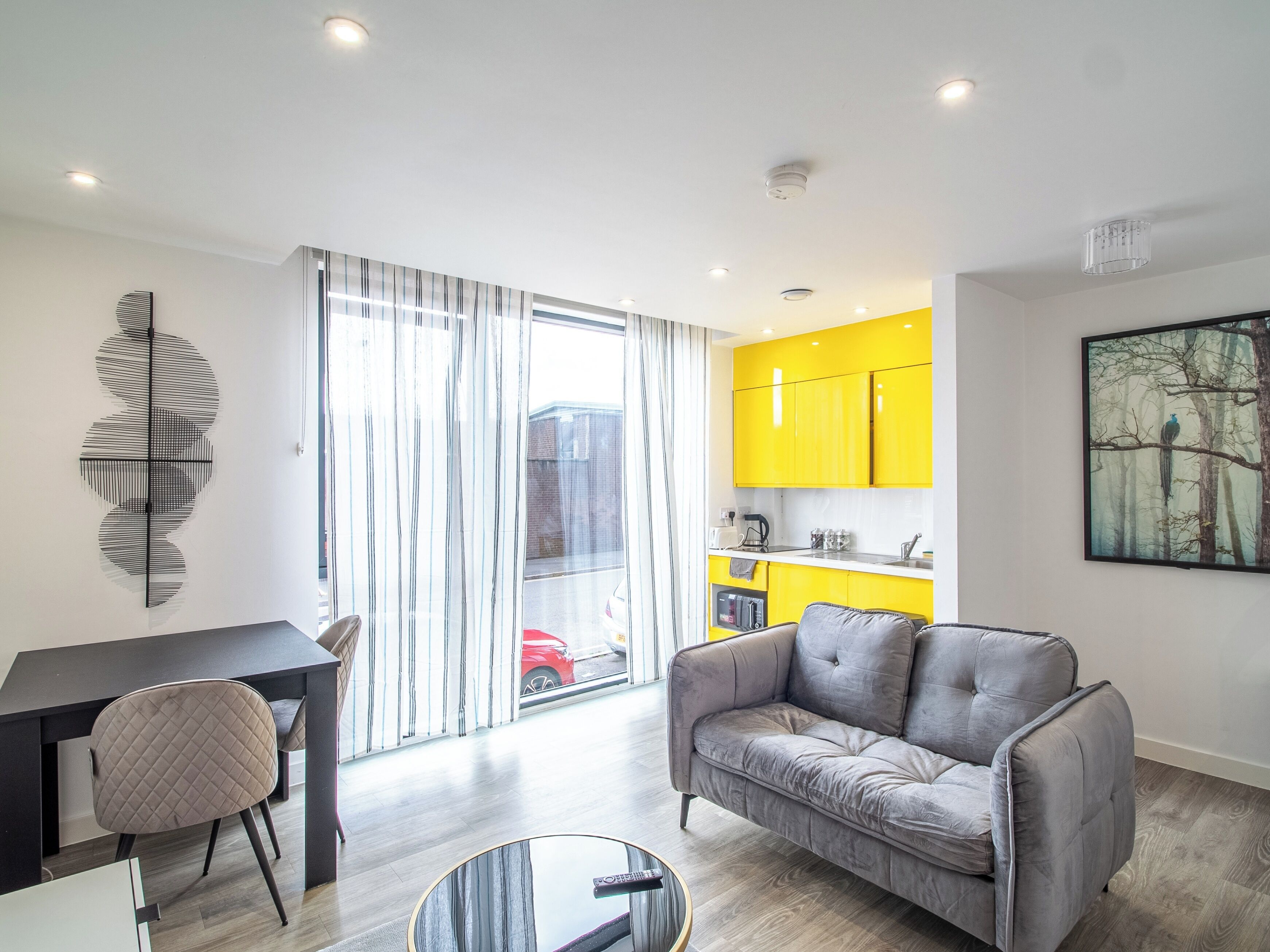 Un salon moderne avec un canapé gris, une table à manger avec une chaise, et une cuisine avec des meubles jaunes.