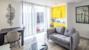 A modern living room with a grey sofa, a dining table with a chair, and a kitchen with yellow cabinets. - Immaculate Studio Apartment in Sheffield City (Sheffield)