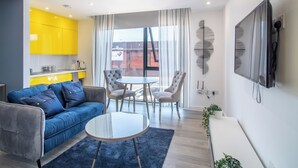 A modern living room with a blue sofa, a round glass coffee table, and a dining area with a white table and chairs. - Deluxe Studio Apartment by Sheffield City Centre (Sheffield)