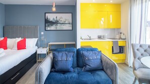 A modern hotel room with a bed, a sofa, a desk, and a bright yellow kitchen. - Deluxe Studio Apartment by Sheffield City Centre (Sheffield)