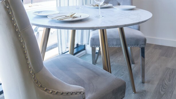 A dining area with a round table, two upholstered chairs, and a television mounted on the wall. - Deluxe Studio Apartment by Sheffield City Centre (Sheffield)