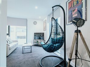 A modern living room with a hanging chair, a tripod, and a television. - Airy and Bright Apartment in City Center (Sheffield)