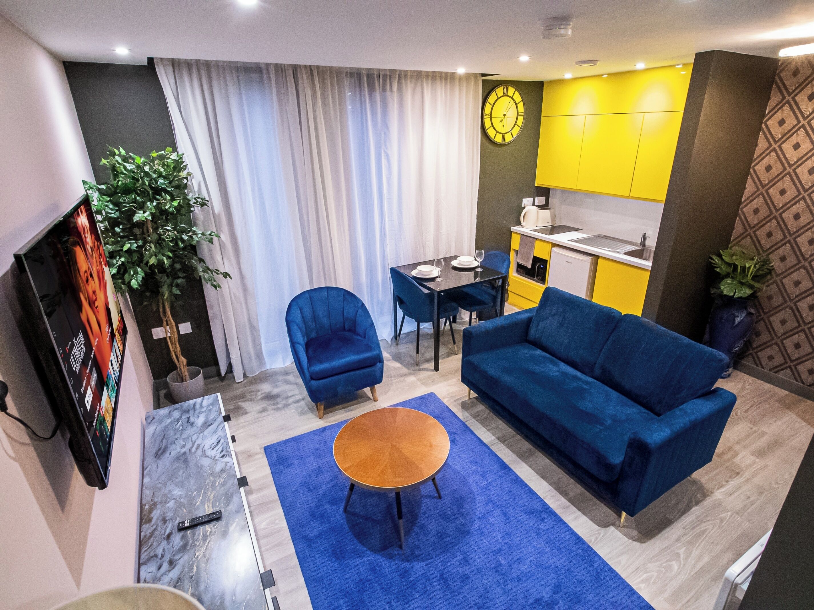 A modern living room with a blue sofa, a small round table, and a TV mounted on the wall.