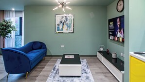 A modern living room with a blue sofa, a coffee table, a painting, and a wall-mounted clock. - Central Sheffield City Apartment (Sheffield)