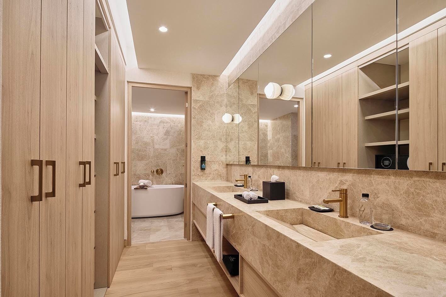 A modern bathroom with a large mirror, two sinks, a bathtub, and wooden cabinets.