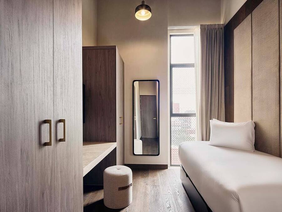 A modern hotel room with a bed, a desk, and a wardrobe.