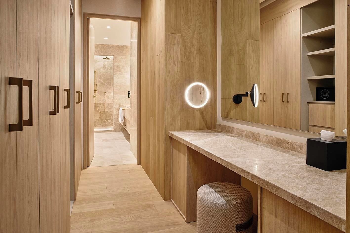 Ein modernes Badezimmer mit Holzschränken, einer Marmorarbeitsplatte und einem Schminkspiegel mit runder Beleuchtung.