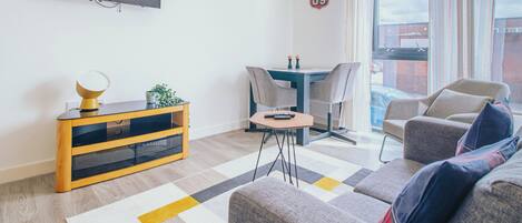 Una sala moderna con un televisor de pantalla plana, una pequeña mesa de comedor y un sofá.